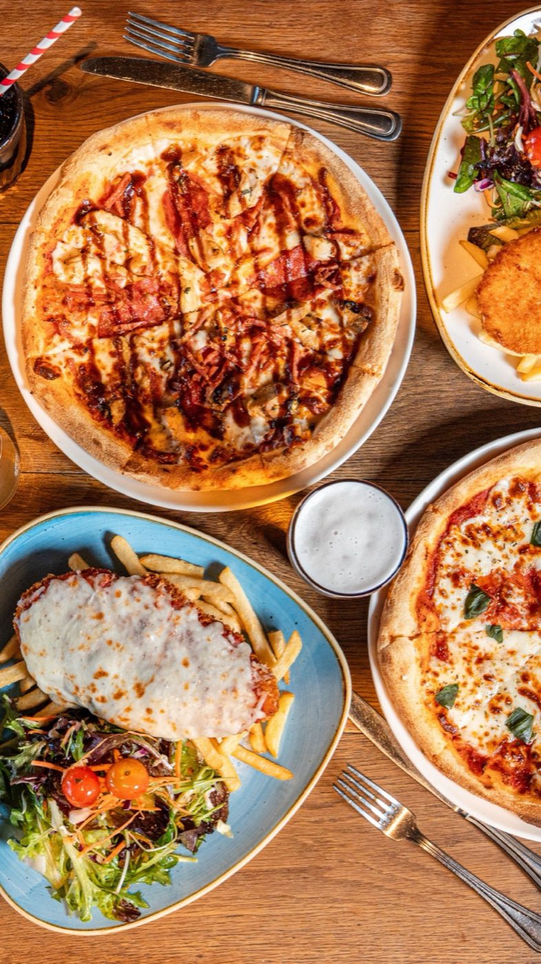 Pizzas and wraps on a timber table, seen from above