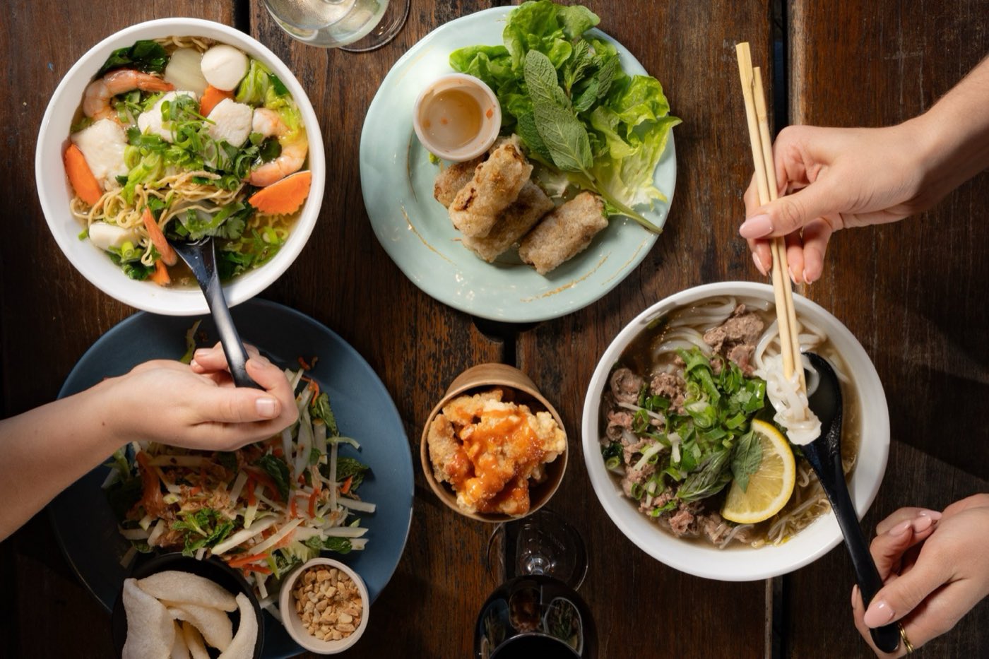Hands with chopsticks reaching over shared Vietnamese bowls