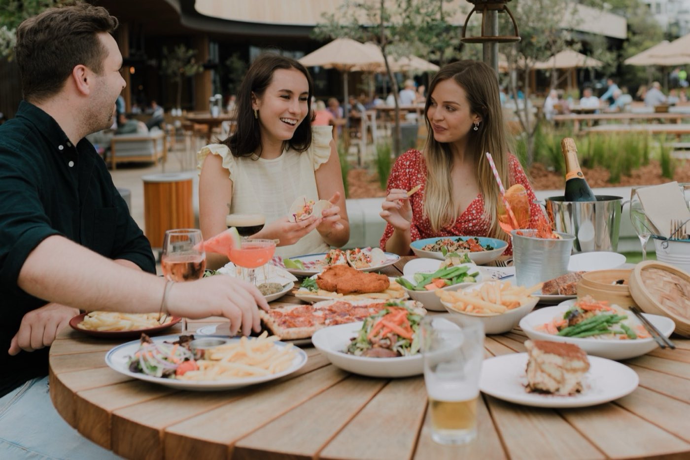Three friends sharing a table of food and drinks on the Ocean Terrace