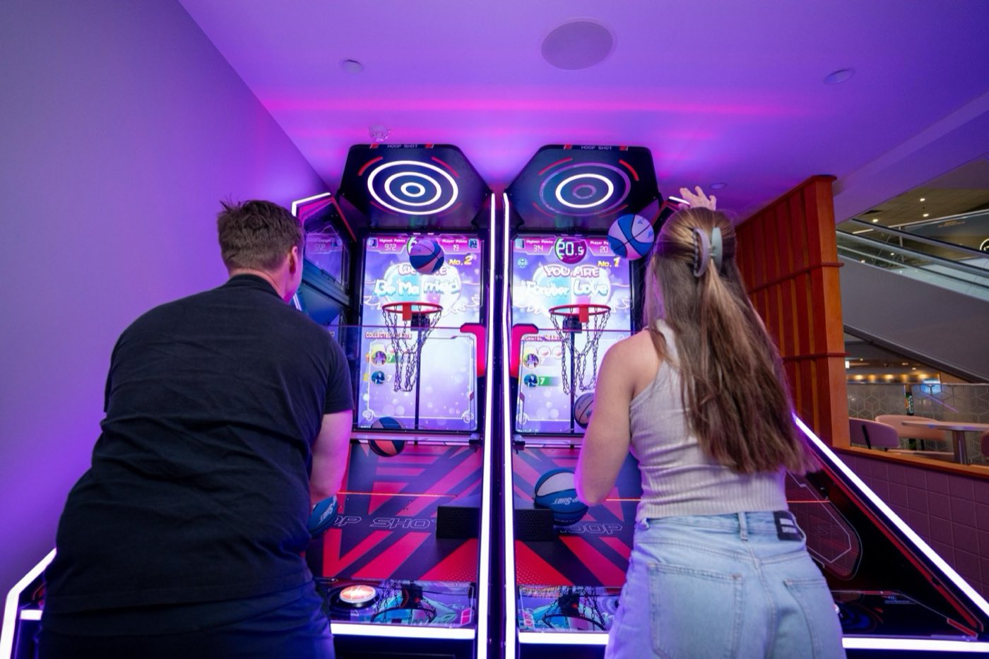 Two people playing arcade basketball under purple neon light